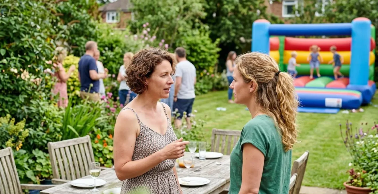 Deux adultes en conversation discrète au premier plan dans un jardin résidentiel, surveillant de loin des enfants jouant sur un château gonflable coloré en arrière-plan
