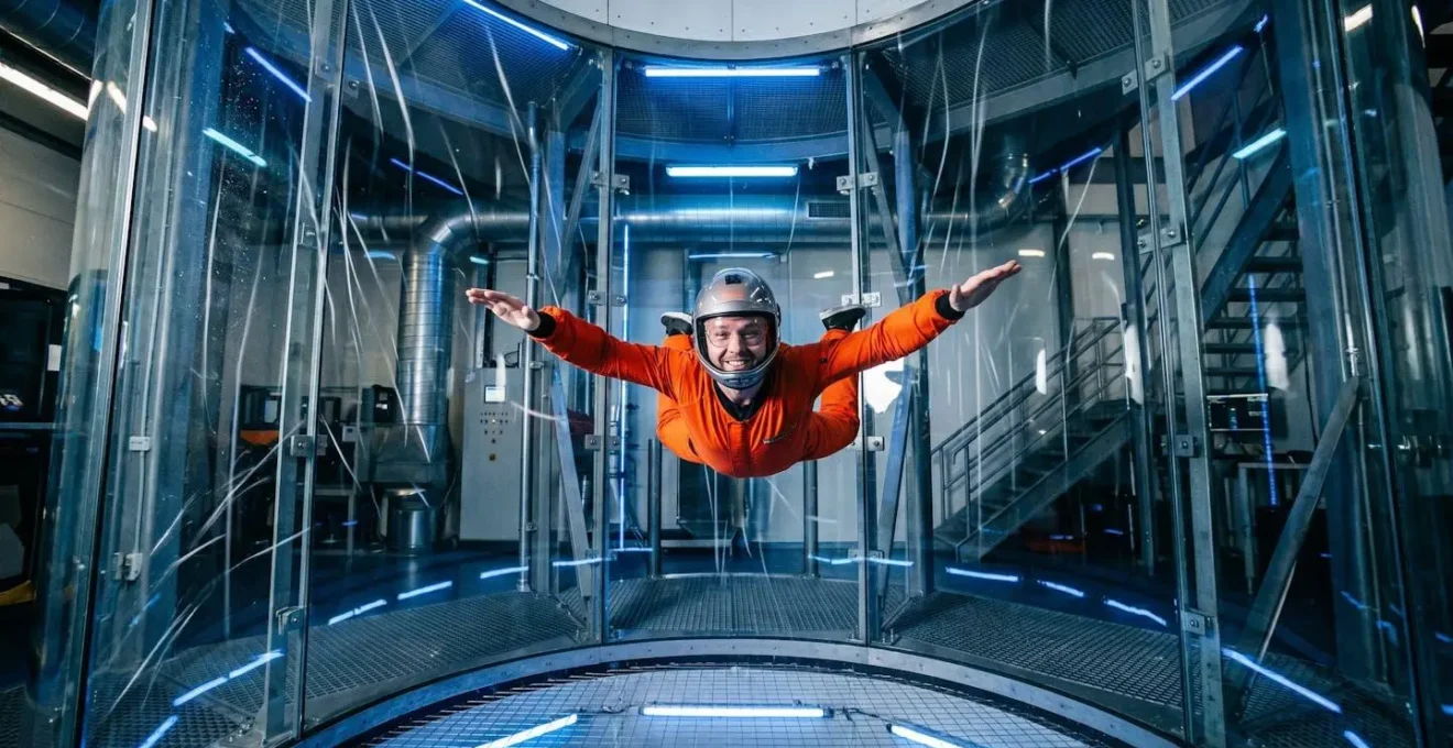 Participant souriant en combinaison de vol flottant dans le tube de la soufflerie verticale.