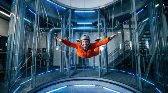 Participant souriant en combinaison de vol flottant dans le tube de la soufflerie verticale.